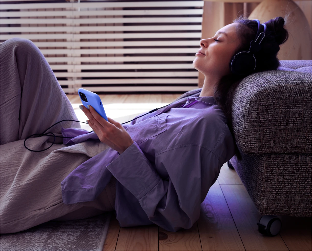 Mulher deitada com fones de ouvido usando o celular de forma relaxada, simbolizando praticidade e autonomia digital