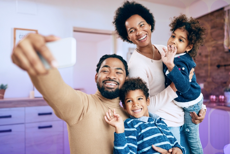 Um homem, sua esposa e seus 2 filhos sorridentes com o homem segurando um celular tirando uma selfie